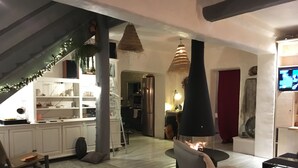 A modern living room with a fireplace, a kitchen area with a staircase, and a dining area.