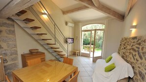 A modern interior with a wooden staircase, a dining area, a sofa with cushions, and a view through a glass door to an outdoor area. - Bastide du Soleil - Studio 2-4 people with private garden (Cannes)