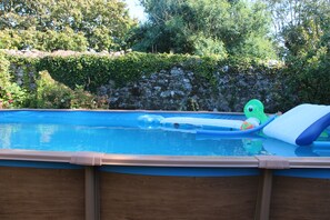 Une piscine hors sol recouverte d’une bâche bleue, entourée d’une terrasse en bois et d’un muret en pierre.