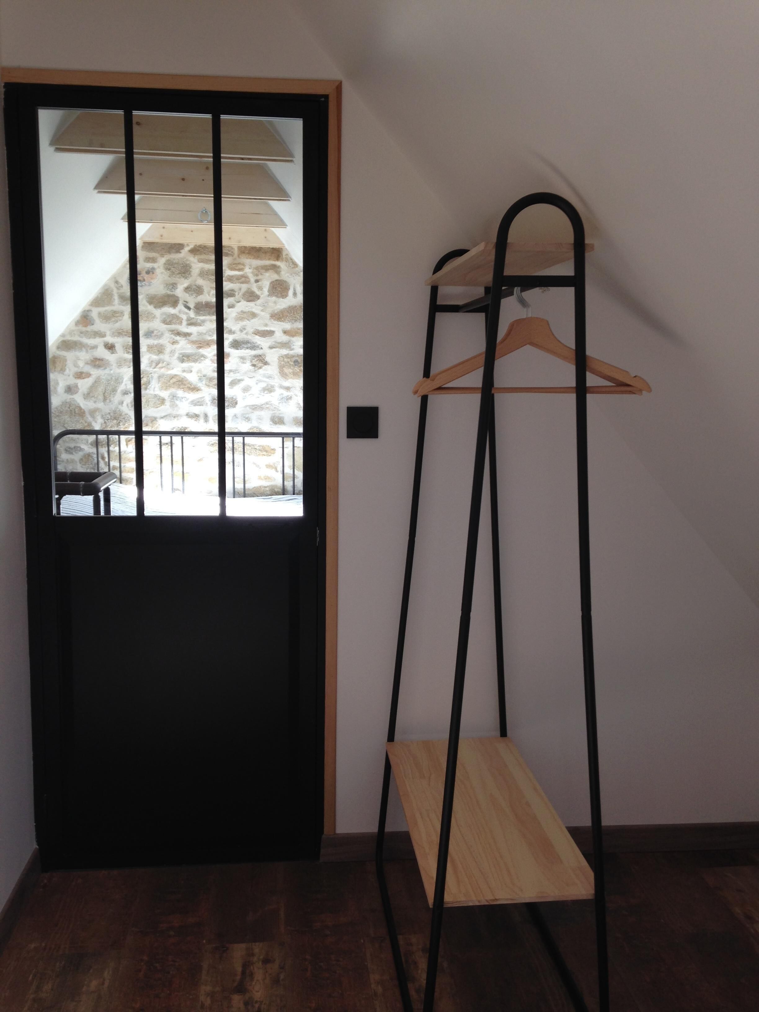 Une pièce avec une porte en bois, un mur en pierre, un porte-manteau en métal noir et un banc en bois.