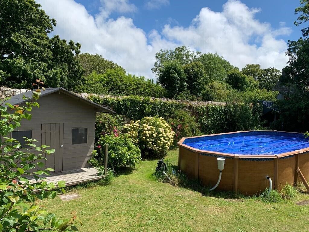 Een achtertuin met een houten zwembad, een tuinhuisje en weelderige begroeiing.