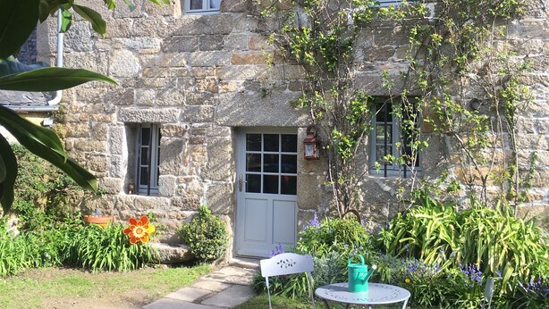 Ein Steinhaus mit einer weißen Tür, ein kleiner Garten mit einer Bank und einem Tisch.