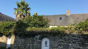 Eine Steinsäule mit einer weißen Tür, die mit der Nummer 21 gekennzeichnet ist, ein Steinhaus mit einem Ziegeldach und eine Palme im Hintergrund.