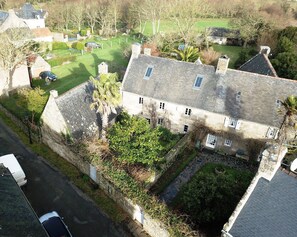 Une vue aérienne d’un bâtiment en pierre doté de nombreuses fenêtres, d’une allée pavée et d’une pelouse bien entretenue.