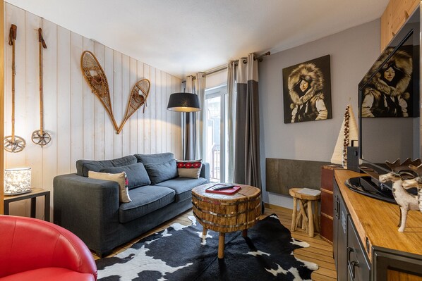 A modern living room with a grey sofa, a round wooden coffee table, a red chair, and a black and white cowhide rug.
