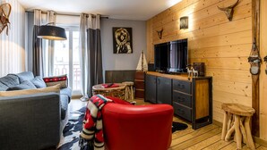 A cozy living room with a sofa, a red chair, a television, and a wooden wall with mounted animal skulls. - COZY APARTMENT RENOVATED CITY CENTER AVENUE LECLERC WIFI AND PRIVATE COVERED PARKING (CAUTERETTS)