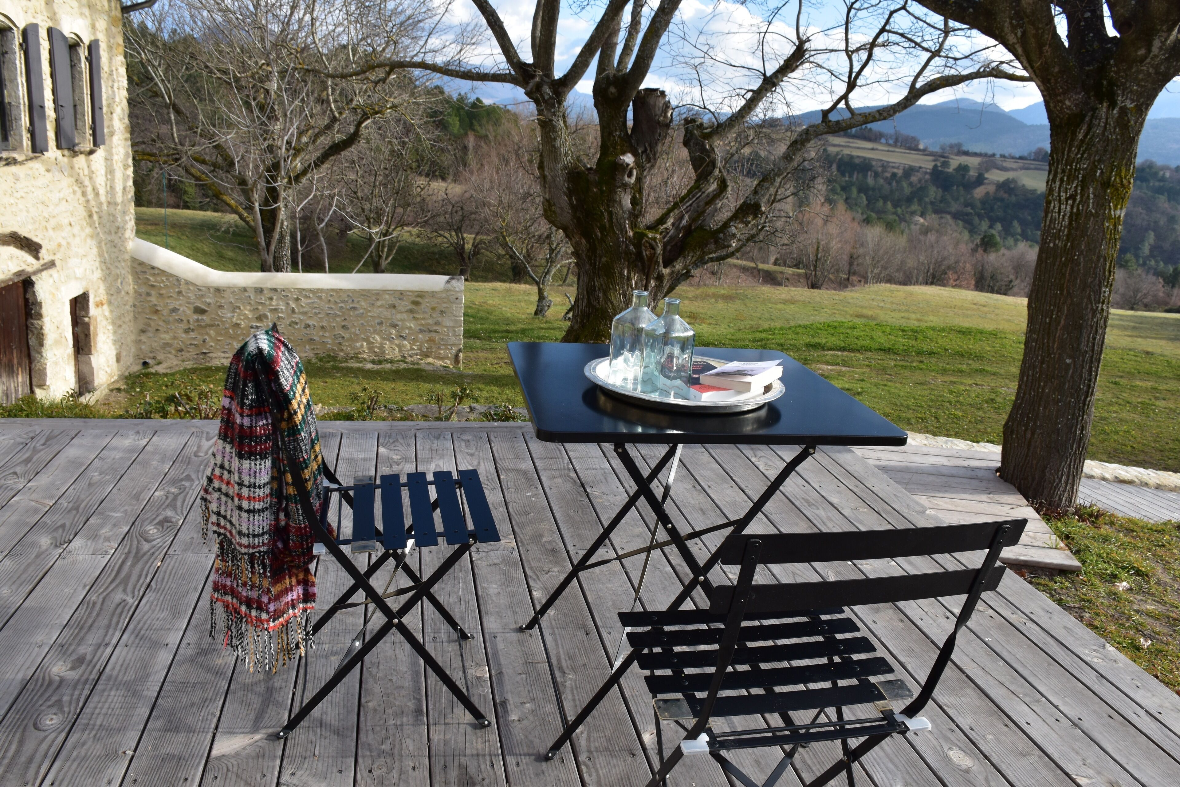 Una terraza de madera con una mesa, sillas y un banco, además de una manta.