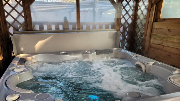 Ein Whirlpool mit Bedienfeld, das 37,0°C anzeigt, umgeben von einer Holzterrasse und einem Holzboden.