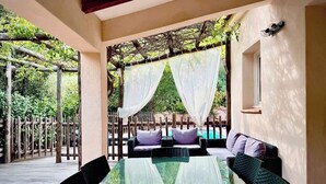 Un área de estar al aire libre con una mesa de vidrio y sillas de mimbre, una terraza de madera y vistas a una piscina.