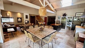Amplia sala de estar con una gran mesa de comedor, asientos cómodos, una cocina con electrodomésticos modernos y una escalera que conduce a un nivel superior.