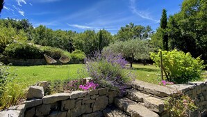 Un jardín con un muro de piedra, una silla mecedora y diversas plantas.