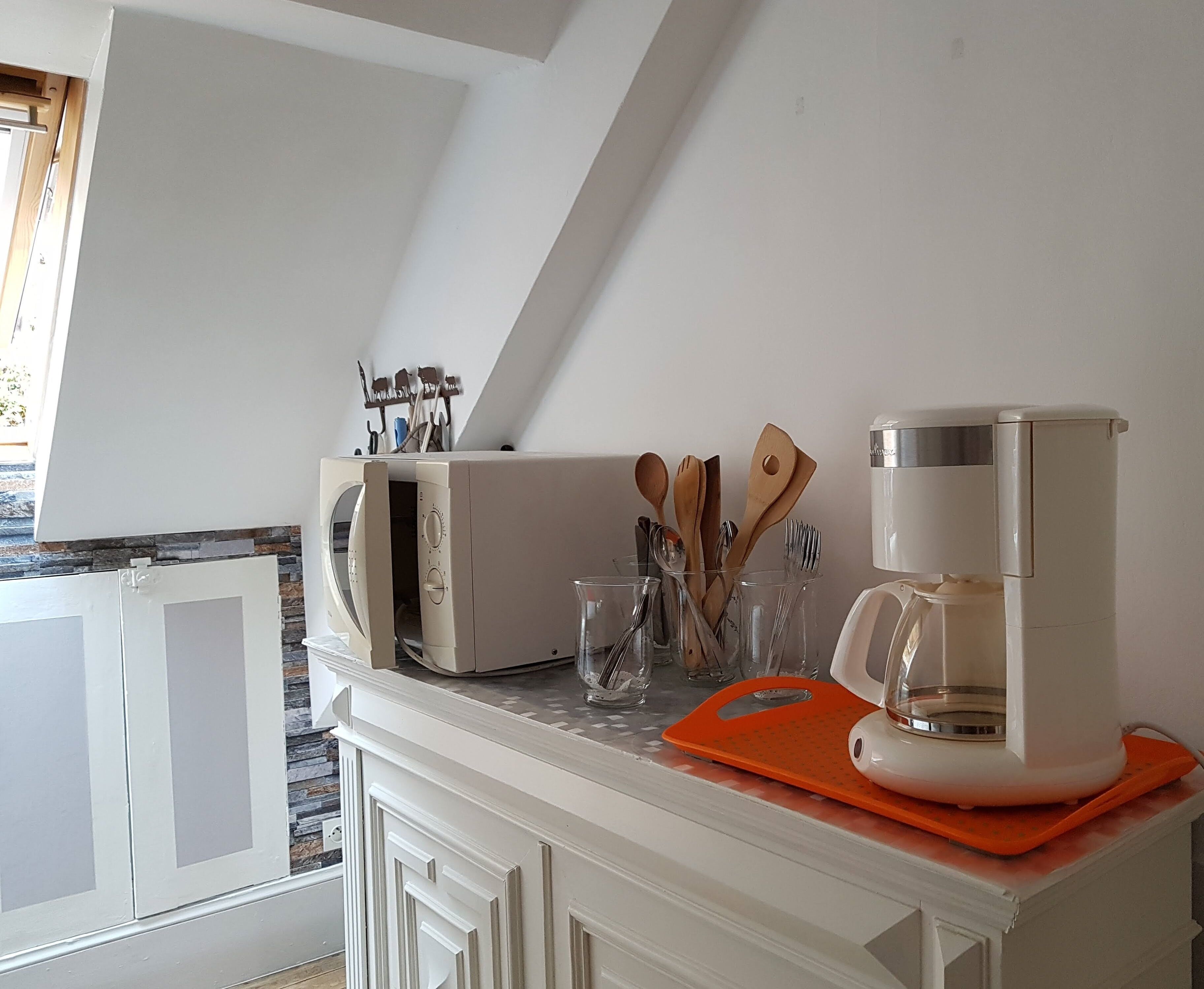 A kitchen with a white countertop, a coffee maker, and wooden utensils.