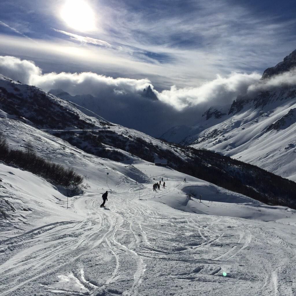 A snowy mountain landscape with ski tracks and a few skiers.