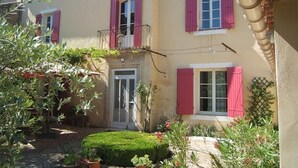 A two-story building with pink shutters, a small balcony, and a neatly trimmed garden. - Provence-Charming house with garden and swimming pool, up to 10 people (Sainte-Cécile-les-Vignes)