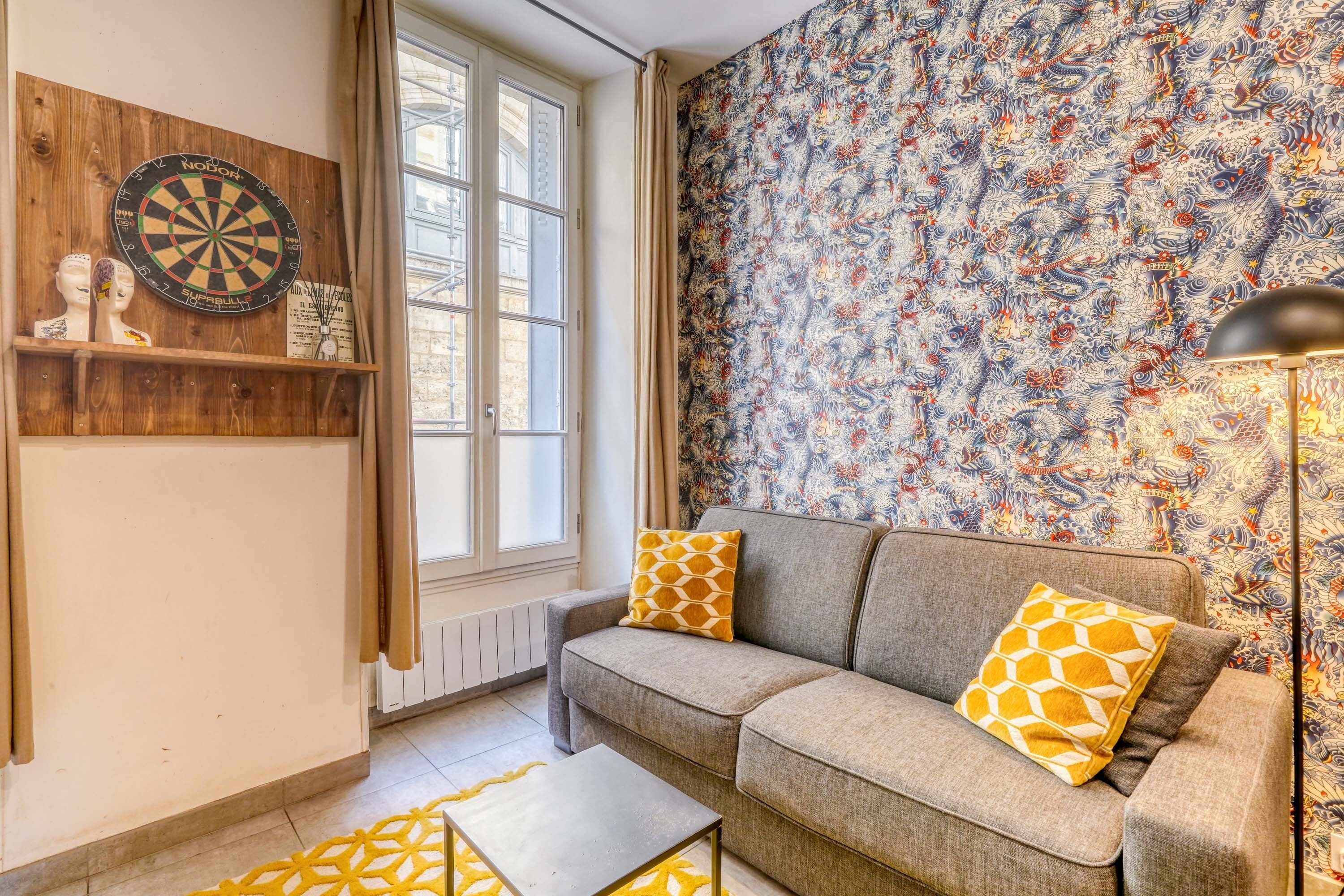 A living room with a sofa, a dartboard, and a patterned wallpaper.