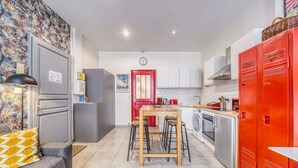 A compact kitchen with a dining area, a red door, and a clock on the wall.
