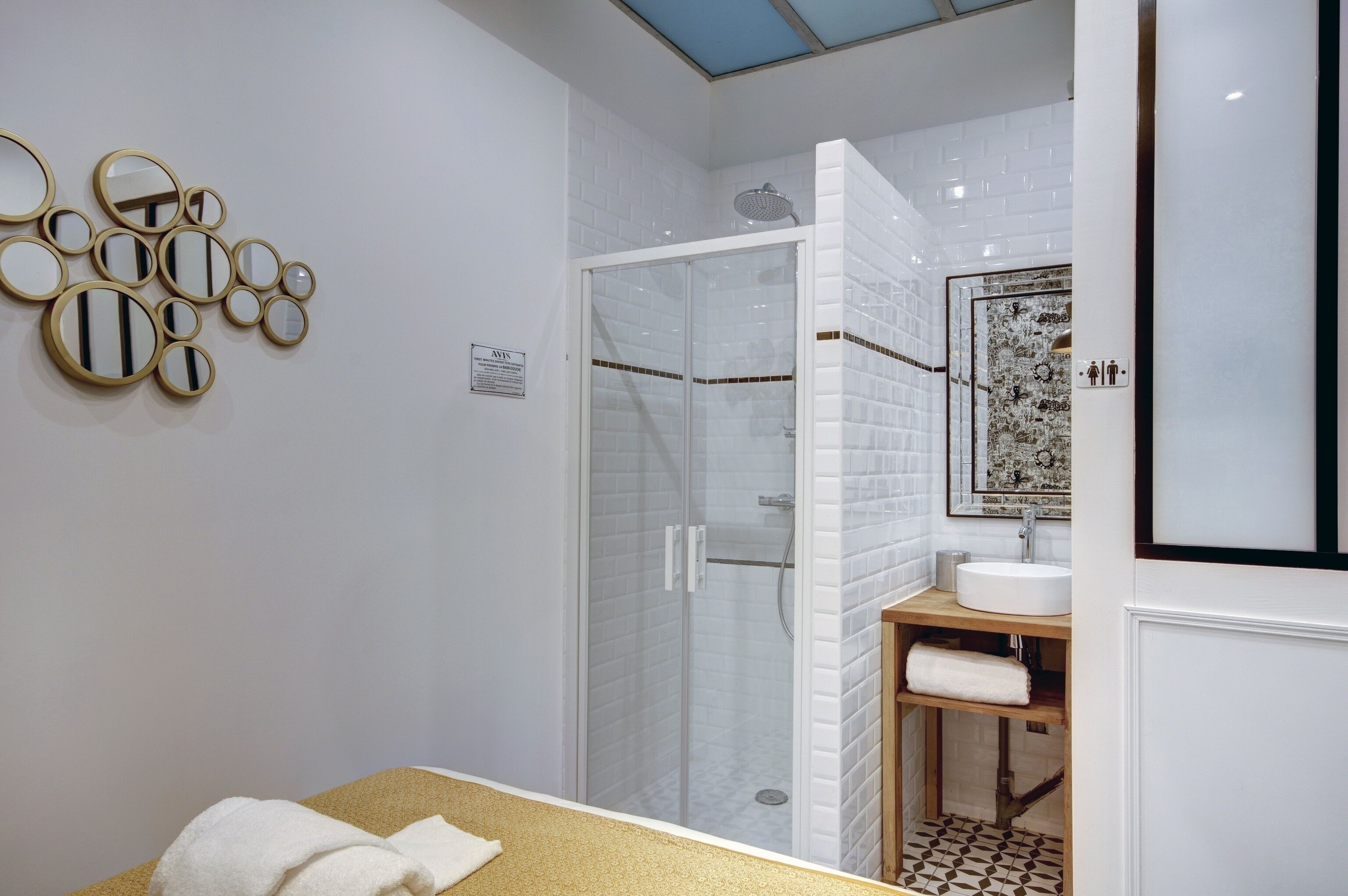 Une salle de bain moderne dotée d’une douche à parois de verre, d’un lavabo avec un miroir au-dessus et d’un mur orné de miroirs ronds.