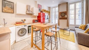 A compact kitchen with a washing machine, a red refrigerator, and a wooden table with stools.