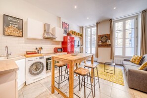 A compact kitchen with a washing machine, a red refrigerator, and a wooden table with stools.