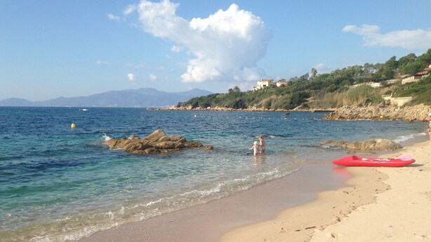 Una playa con agua cristalina, un kayak rojo y huellas en la arena.