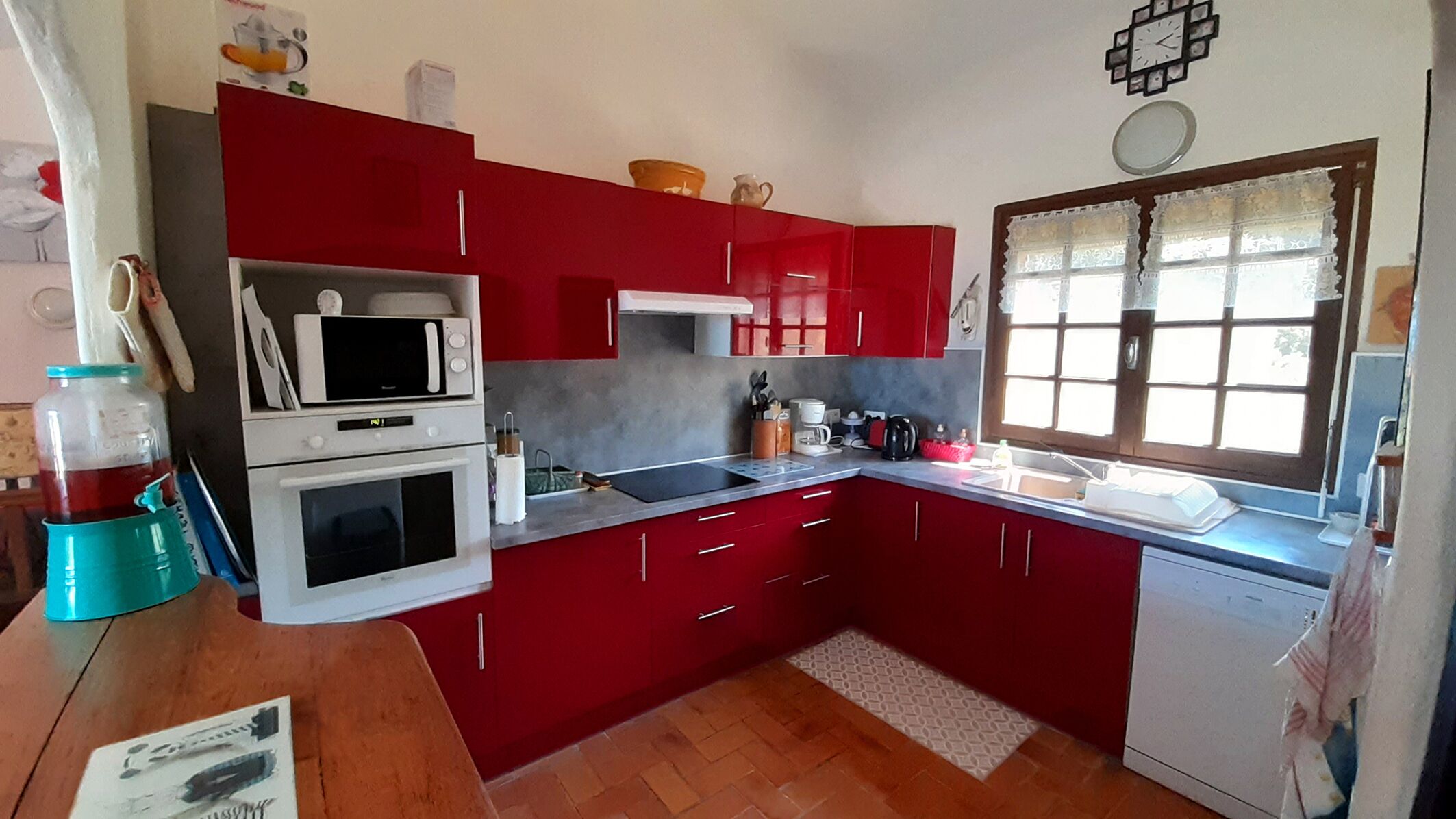 Une cuisine de taille réduite avec des placards rouges, un four à micro-ondes, une cuisinière et un évier.