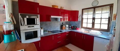 Une cuisine de taille réduite avec des placards rouges, un four à micro-ondes, une cuisinière et un évier.