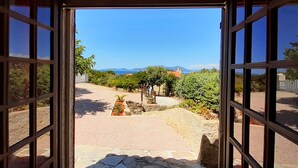Vista desde una puerta abierta a un patio con un sendero de piedra, plantas en macetas y una cadena montañosa en la distancia.
