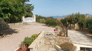 Un camino de piedra conduce a una entrada portonada, con vistas a montañas y un paisaje costero.