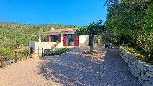 Una casa pequeña con camino de grava, rodeada de vegetación y colinas.
