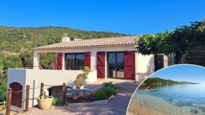 Una casa costera con techo de tejas, contraventanas rojas y un camino de piedra que lleva a una puerta.