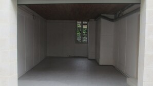 Un couloir propre et dégagé, avec un sol et des murs carrelés de blanc, un plafond en bois et une petite fenêtre d’où l’on aperçoit de la verdure.