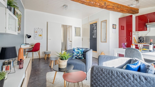 Un salon moderne comprenant un canapé, des fauteuils, une table basse et un coin repas avec un buffet rouge et un comptoir de cuisine.