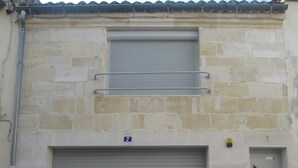 Un bâtiment doté d’un garage avec une porte à volet roulant, d’une petite fenêtre ornée d’une rambarde en métal et d’une porte au motif géométrique.