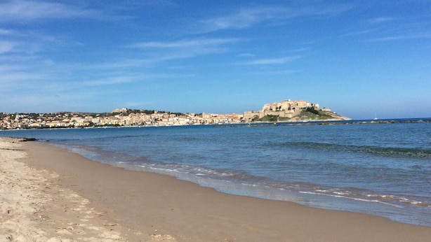 A beach with a sandy shore and a distant view of a fortified hill with buildings.