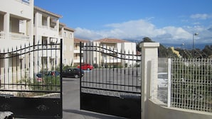 A gated residential area with a paved road, parked cars, and multi-story buildings with balconies.