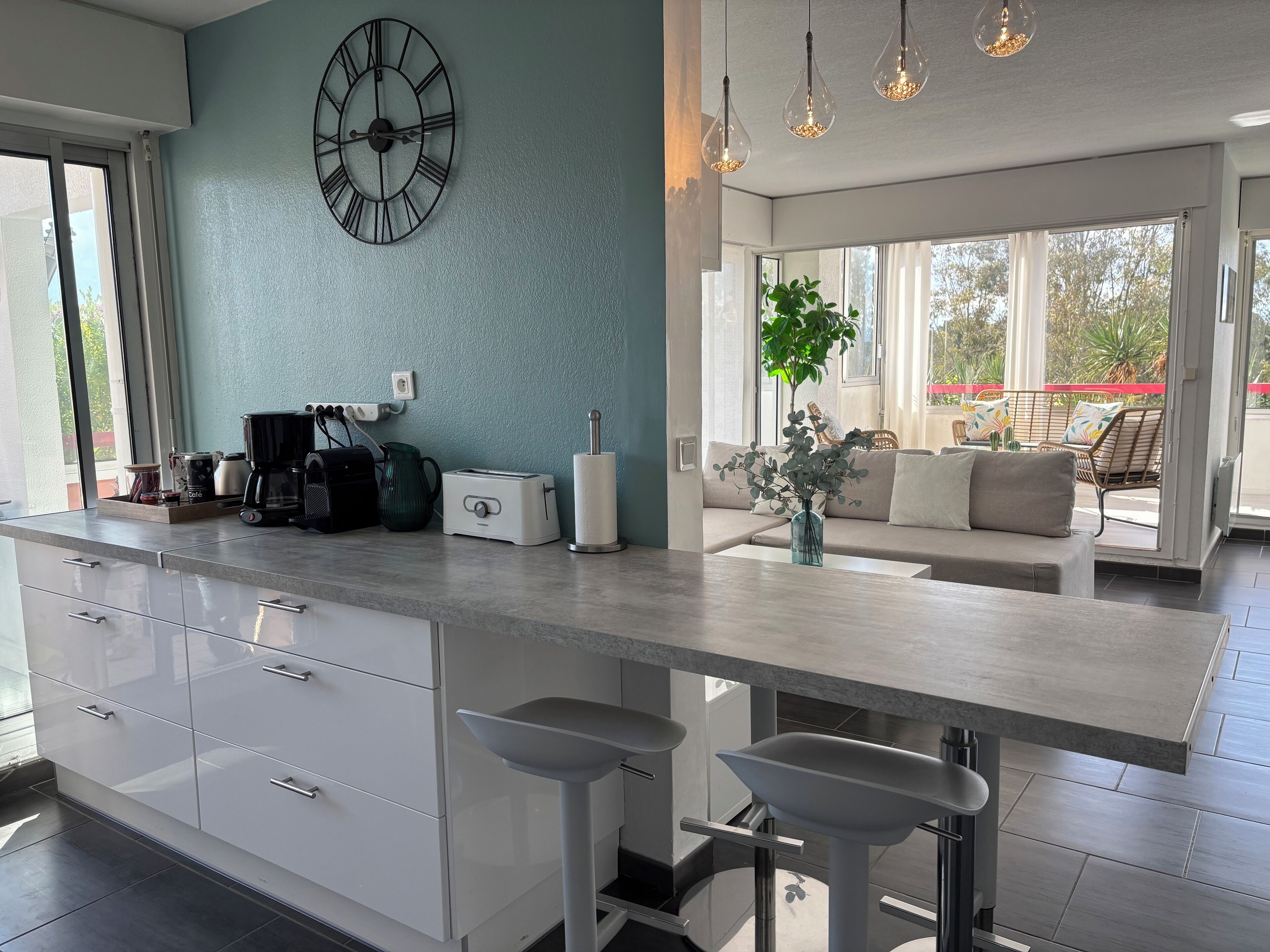 Una cocina moderna con una isla grande, taburetes de bar, una cafetera y un reloj en la pared.