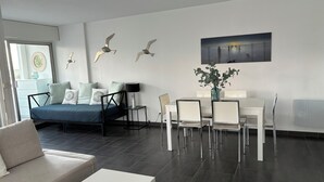 A modern hotel room with a bed, a dining area with chairs, a table, and a vase with plants. - Canet Sud Very nice apartment of 85 m² 150 m from the beach Parking Air conditioning Wi-Fi (Canet-En-Roussillon)