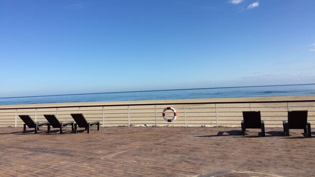 A beachside area with a wooden deck, several lounge chairs, a lifebuoy, and a clear view of the ocean. - Canet Sud Very nice apartment of 85 m² 150 m from the beach Parking Air conditioning Wi-Fi (Canet-En-Roussillon)