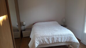 Un dormitorio con una cama, una mesita de noche, una lámpara y un espejo.