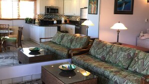 A living room with a sofa, a dining table, and a kitchen in the background. - KIHEI KAI NANI #6-246  Beautiful open view with  Ocean/Pool in Tropical Garden (Kihei)