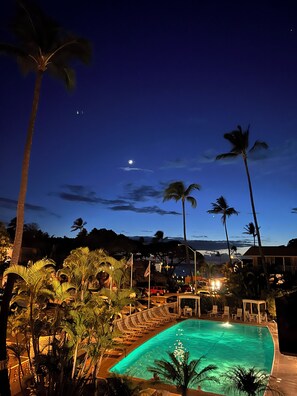 A nighttime view of a pool area with lounge chairs and palm trees. - KIHEI KAI NANI #6-246 Beautiful open view with Ocean/Pool in Tropical Garden (Kihei)