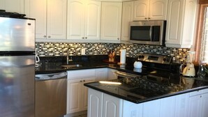 A modern kitchen with white cabinets, a stainless steel refrigerator, a microwave, and a black countertop. - KIHEI KAI NANI #6-246  Beautiful open view with  Ocean/Pool in Tropical Garden (Kihei)