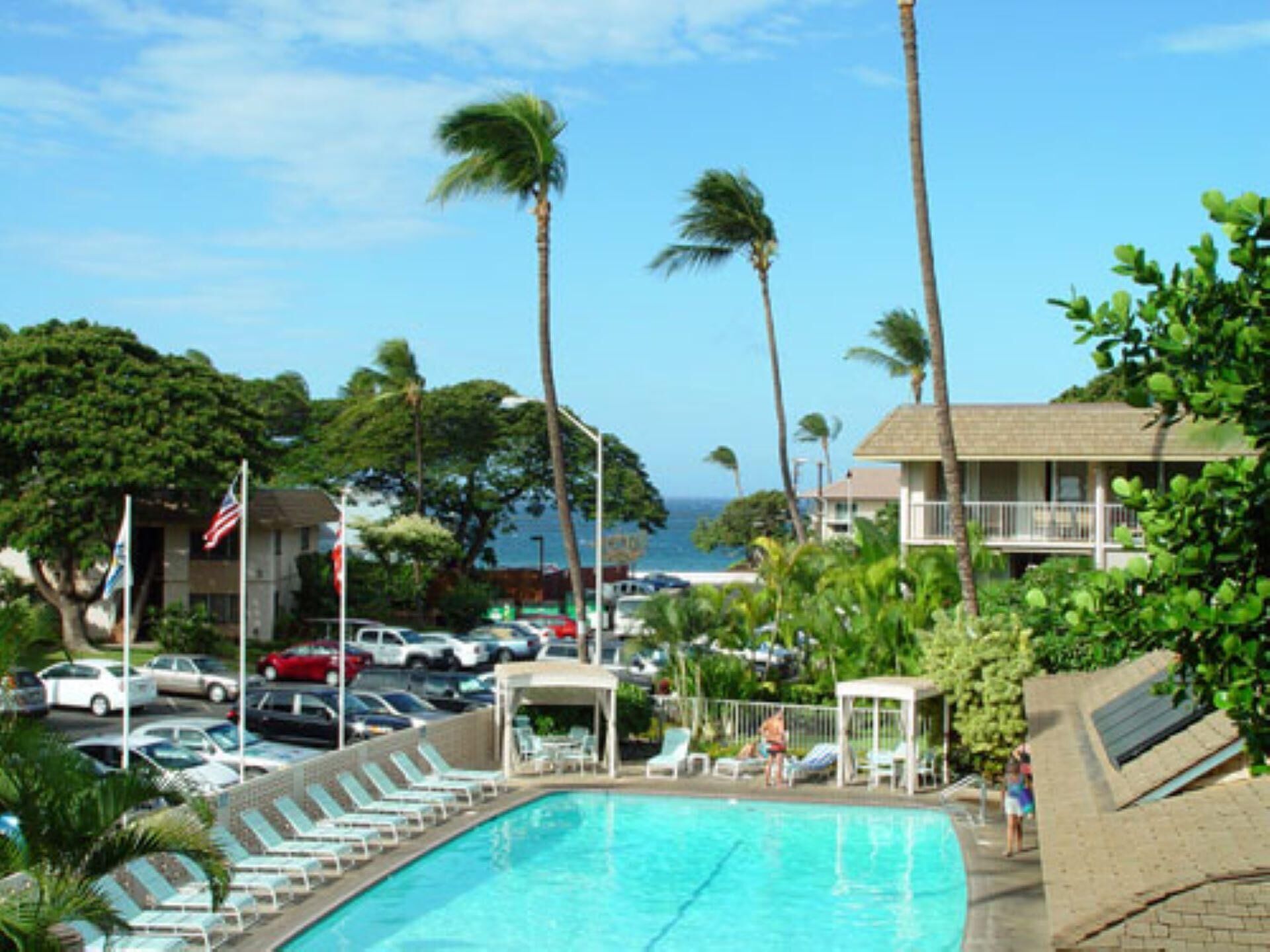 A pool area with lounge chairs, a covered seating area, and a view of the ocean.
