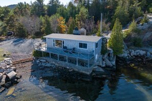 Eine Hütte auf Stelzen über dem Wasser, umgeben von Bäumen und einer felsigen Küstenlinie.
