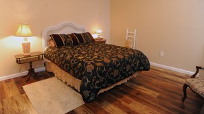 A bedroom with a large bed, two bedside tables with lamps, a chair, and a wooden floor. - COOL COTTAGE AT 4800 FT  SLEEPS 8. GOOGLE MAP IS NOT CORRECT 10 MILES TO B ROCK (Blowing Rock)
