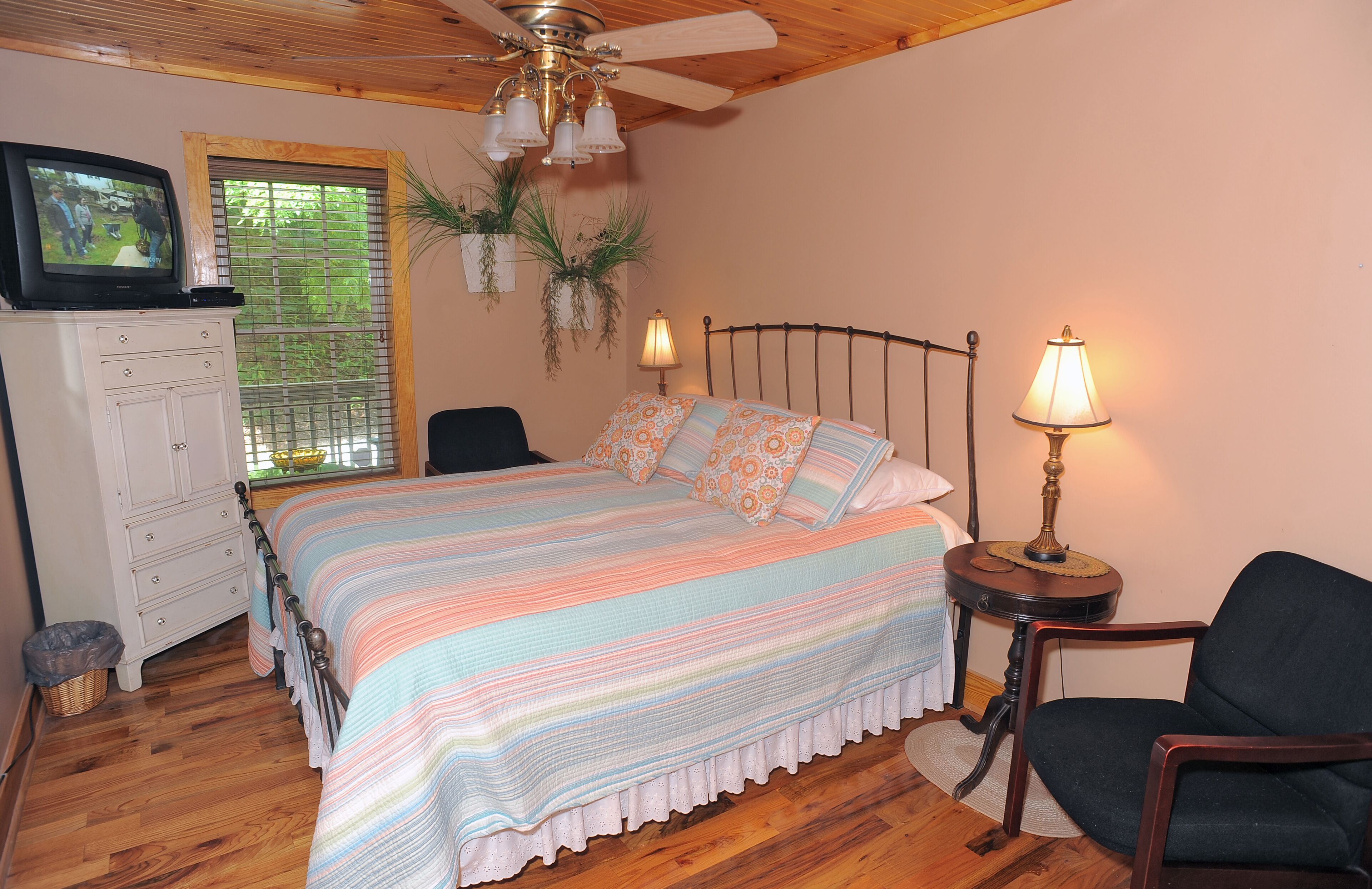 A bedroom with a bed, a television on a dresser, a lamp, and a chair.