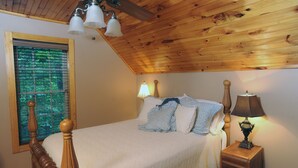 Een slaapkamer met een houten plafond, een bed met een witte dekbedovertrek, twee bedlampen en een raam met zonwering.