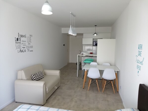 A modern, compact living space with a sofa, dining table, and chairs. There are wall decorations with motivational phrases. - Independencia 1302 9C by HB (Buenos Aires)