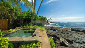 Une piscine dotée d’une terrasse en bois, entourée de plantes tropicales et bordée d’une côte rocheuse.