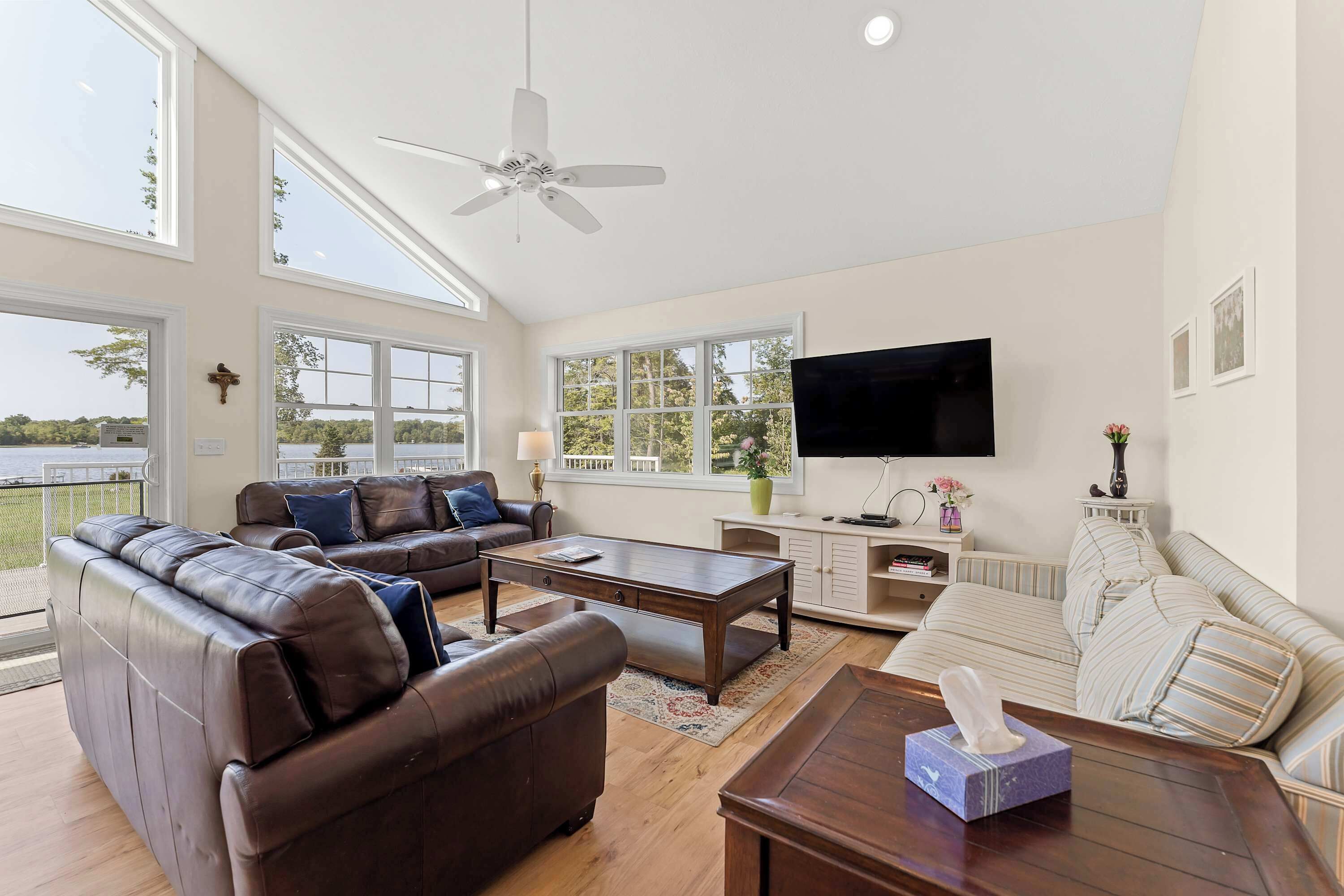 Ein geräumiges Wohnzimmer mit großem Fenster, Deckenventilator, Flachbildfernseher und einer Couch.
